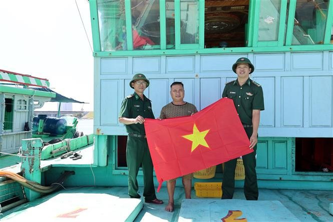 Des officiers et soldats du poste de garde-frontière de Son Tra (Commandement de la Garde-frontière de la ville de Da Nang) remettent le drapeau national à un bateau de pêche local. Photo : VNA
