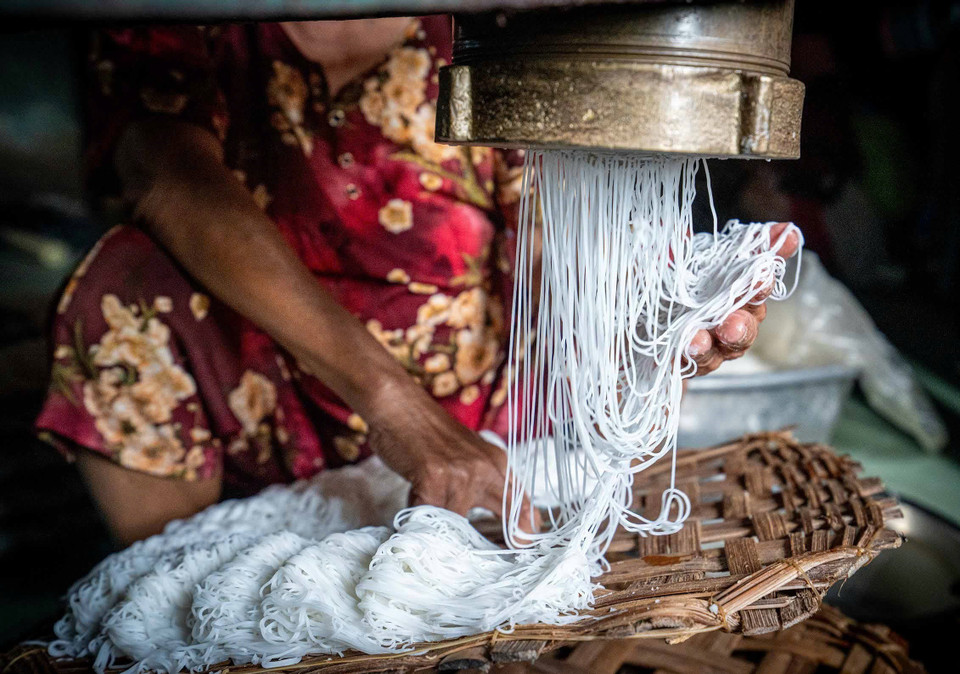Une fois extrudée en fins filaments, la pâte est travaillée avec agilité : l'artisan sépare les brins manuellement pour former des bouquets de nouilles calibrés, qu'il dépose soigneusement sur un support en bambou. Photo : VNA