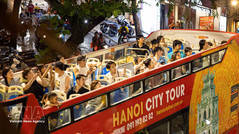 Des touristes vietnamiens et étrangers admirent la vue panoramique sur Hanoï de nuit depuis le pont supérieur d'un bus touristique Hanoi City Tour.