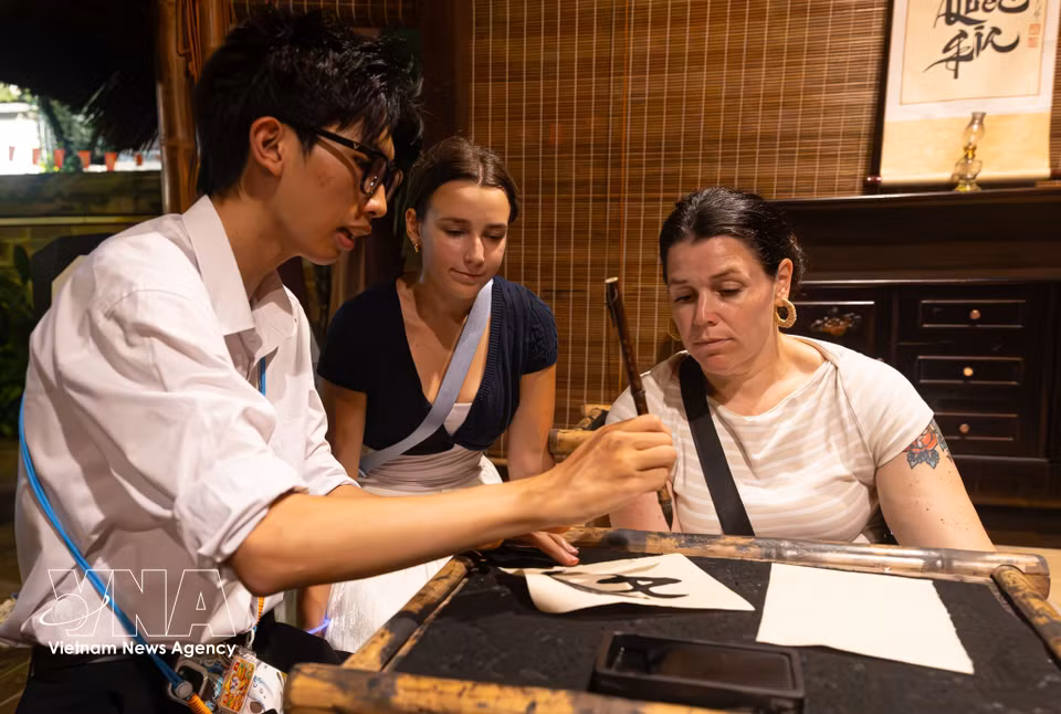 Des touristes internationaux s'initient avec enthousiasme à l'art de la calligraphie au pinceau sous la conduite d'un guide culturel.