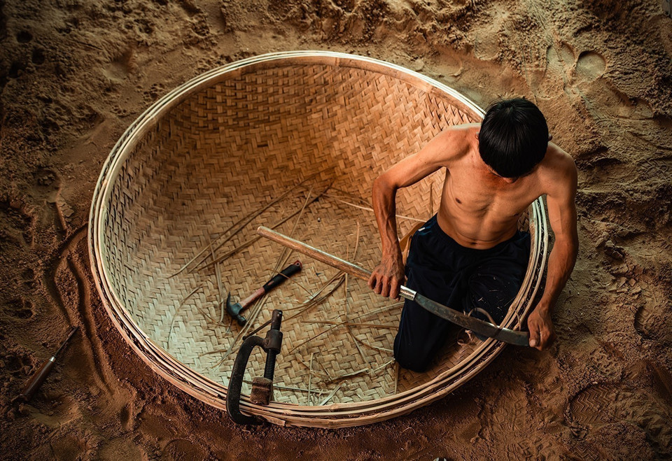 Pour former le moule, l’artisan creuse un trou circulaire dans le sol, y place le fond du bateau préalablement tressé, puis poursuit les étapes suivantes. Photo: VNA