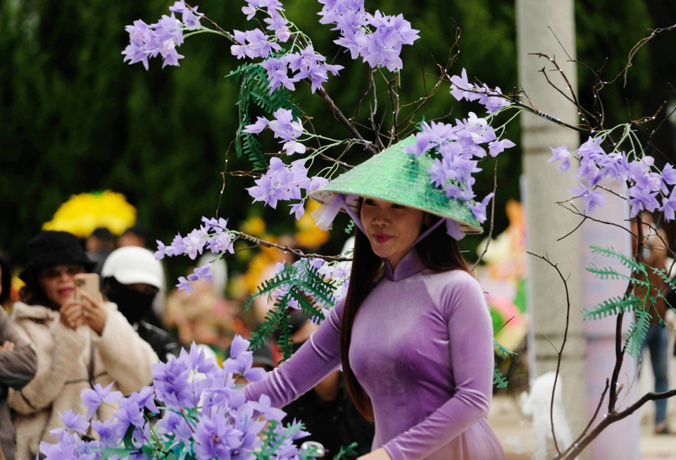 Une charmante enseignante avec des fleurs du flamboyant bleu en papier accompagnées d'un chapeau conique et d'un ao dai. Photo: VNA