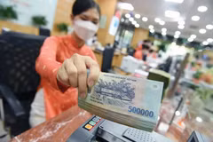 Une employée de banque compte des liasses de billets à un guichet. Photo : tinnhanhchungkhoan.vn