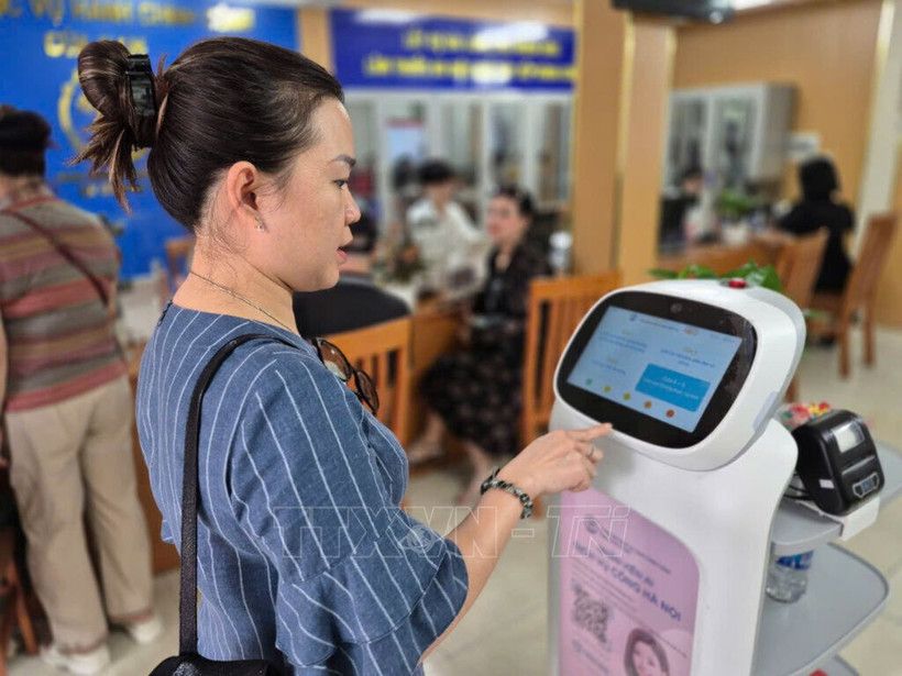 Les gens font l'expérience de robots IA appliquant la technologie de l'intelligence artificielle pour soutenir les procédures administratives dans le quartier de Cua Nam, dans la ville de Hanoi. Photo : VNA