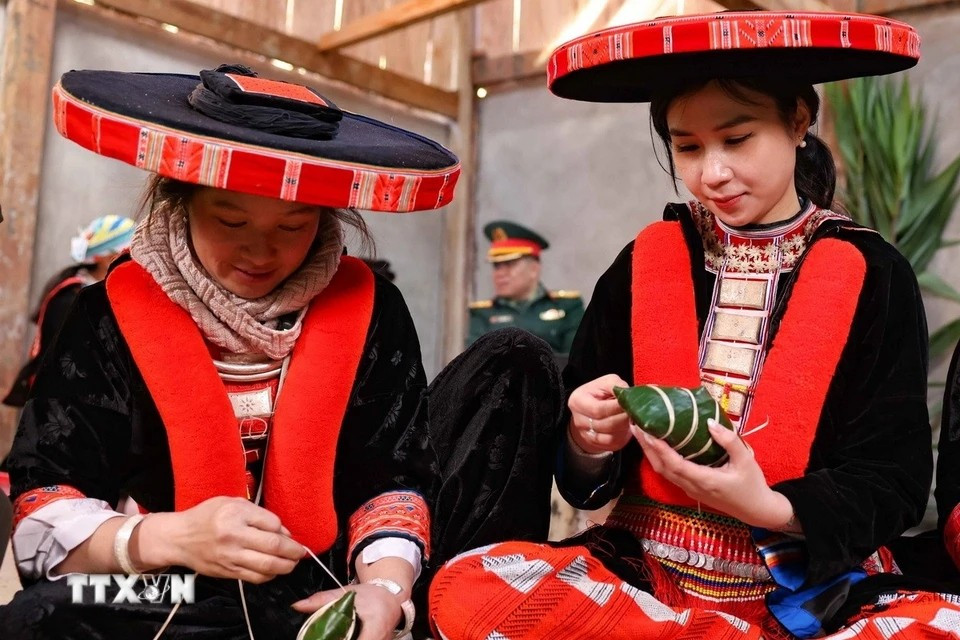 Une touriste hanoïenne (droite), vêtue d'un magnifique costume traditionnel Dao Rouge du district de Nguyen Binh, s'initie avec passion à l'art ancestral de l'emballage des banh chung gù. Contrairement au banh chung carré, le banh chung gù a une forme plus arrondie, légèrement bombée au centre, d'où son nom "gù" qui signifie "bossu" en vietnamien. (Photo : Thanh Tung/VNA)
