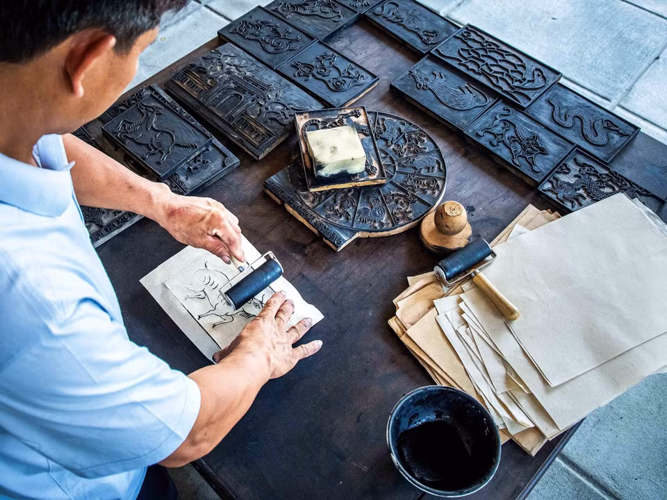 À partir des planches de bois gravées, l'artisan applique uniformément sur le papier une encre noire fabriquée à base de cendres de paille et de feuilles argentées. Photo : VNA