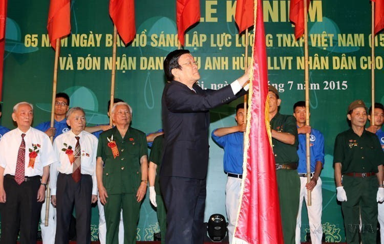 Le président de la République Truong Tân Sang remet le titre de Héros des forces armées populaires à l’Équipe des Jeunesses volontaires n°36 lors de la cérémonie commémorative du 65e anniversaire de la fondation de la Force des Jeunes volontaires du Vietnam (15 juillet 1950–2015). Photo : VNA