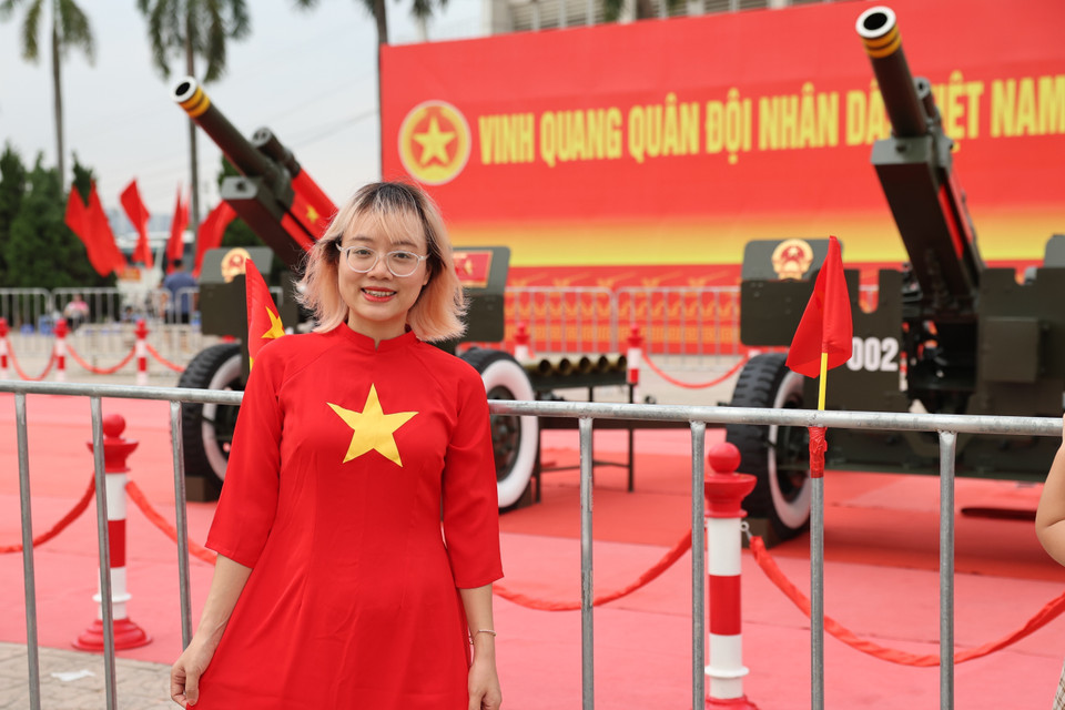 Une jeune femme vêtue d’un ao dài orné du drapeau vietnamien sourit radieusement à côté des canons. Photo : VNA