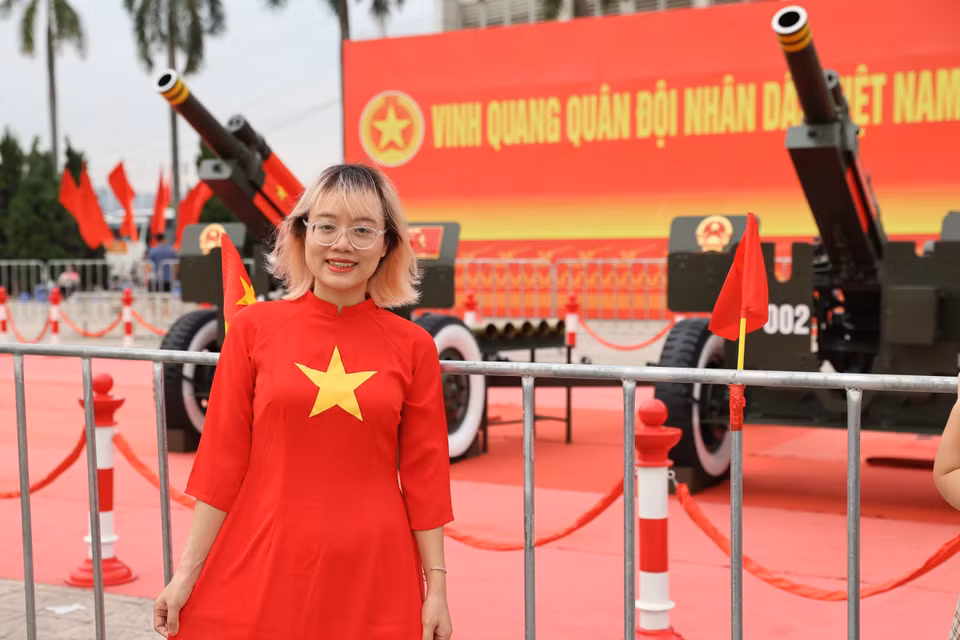 Une jeune femme vêtue d’un ao dài orné du drapeau vietnamien sourit radieusement à côté des canons. Photo : VNA