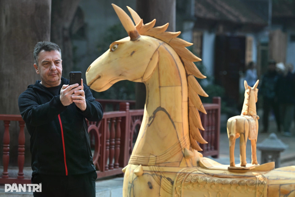 De nombreux visiteurs, parmi lesquels des touristes étrangers, se montrent enthousiastes et prennent volontiers des photos souvenirs aux côtés des sculptures de chevaux en bois exposées.