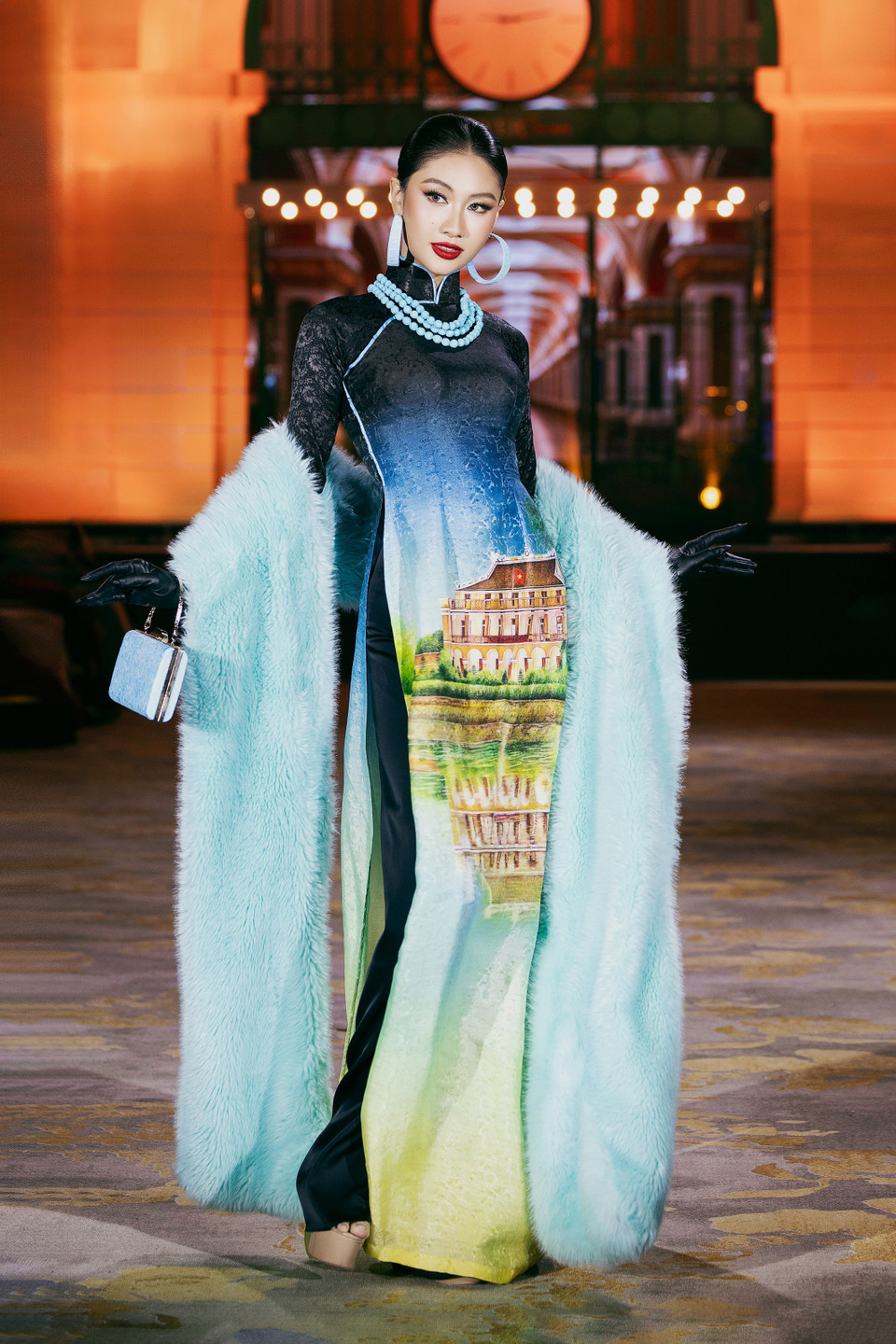 Chaque tenue met en valeur des œuvres architecturales et des paysages du monde entier. Sur la photo, Miss Cosmo Vietnam 2025, Nguyên Hoàng Phuong Linh, attire tous les regards dans un ao dài orné d’une image du quai de Nhà Rông.