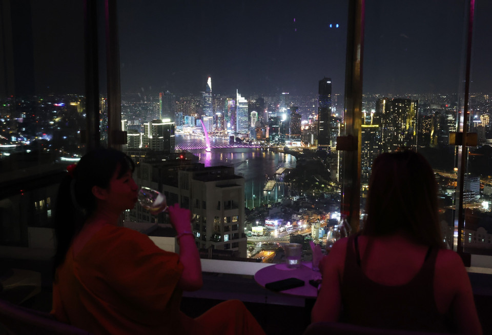 Des clients profitent de l'espace Club Lounge du Vinpearl Landmark 81 pour admirer la vue panoramique nocturne du centre-ville.