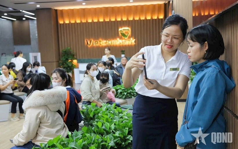 Des employés de la Banque commerciale par actions pour le commerce extérieur du Vietnam (Vietcombank) guident des clients dans la réalisation de l’authentification biométrique. Photo : Quân đội nhân dân