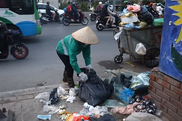 Un agent d'entretien ramasse les ordures dans une décharge sauvage à Hanoï. Photo VNA