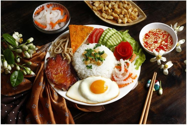 Le Com Tam est généralement servi avec une variété de viandes grillées, comme de savoureuses côtelettes de porc ou de la peau de porc effilochée. Les œufs au plat ou les omelettes apportent de la richesse, tandis que des légumes frais comme le concombre et des légumes marinés apportent un délicieux croquant. Source: izitour.com