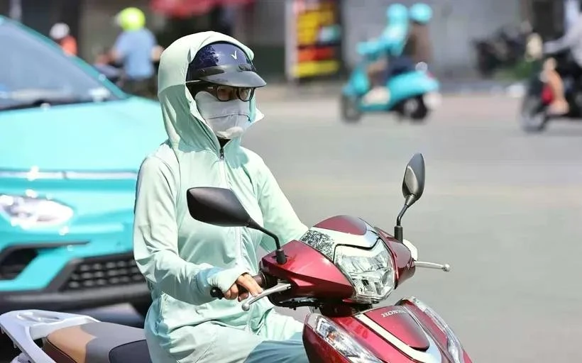 Une motocycliste se couvre le visage d’un tissu pour s’abriter de la chaleur. Photo : VNA