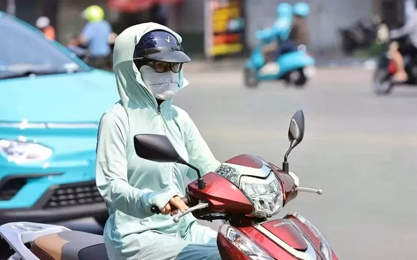 Une motocycliste se couvre le visage d’un tissu pour s’abriter de la chaleur. Photo : VNA