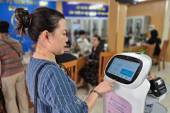 Les gens font l'expérience de robots IA appliquant la technologie de l'intelligence artificielle pour soutenir les procédures administratives dans le quartier de Cua Nam, dans la ville de Hanoi. Photo : VNA