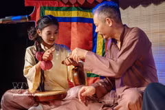 Une jeune s’initie à un instrument de musique auprès d'un artisan. Photo : VNA