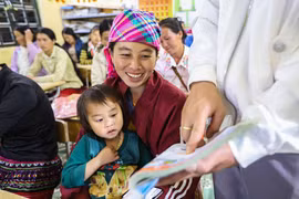 Hang Thi Cha, accompagnée de sa fille, s’exerce à la lecture avec son enseignant à l’aide d’un manuel de vietnamien de première année. Photo : VNA