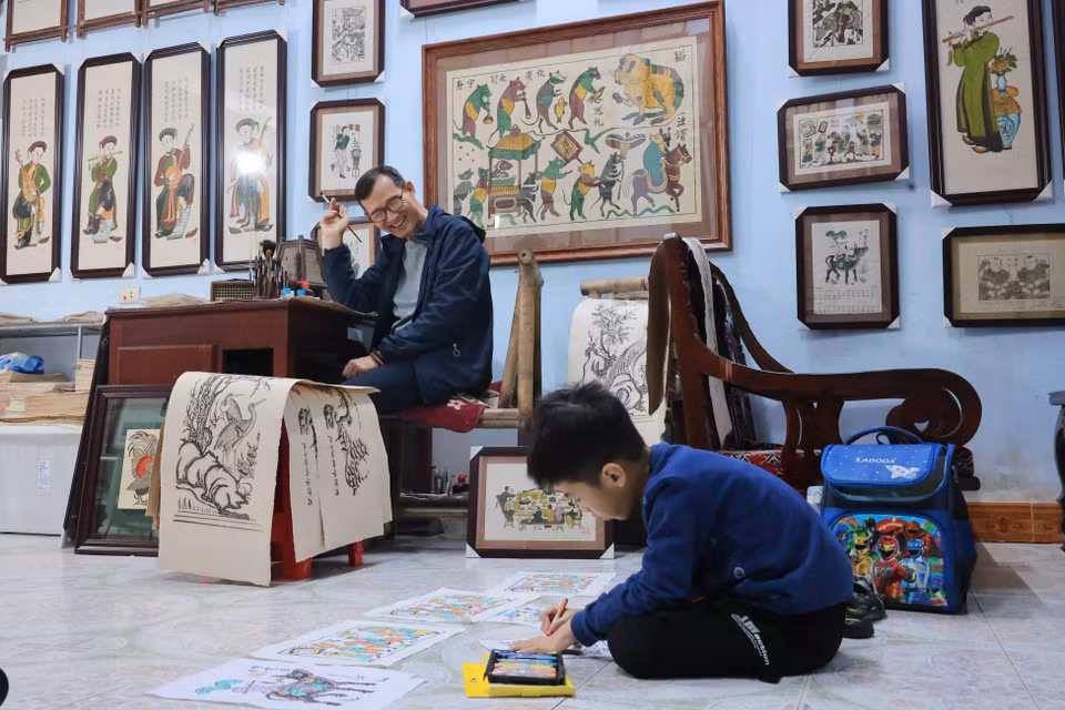 L'artisan émérite Nguyên Huu Qua est rempli de fierté de voir son petit-fils, Nguyen Huu Minh Dang, perpétuer la tradition familiale en s'initiant à l'art ancestral des estampes populaires de Dông Hô. Photo : VNA