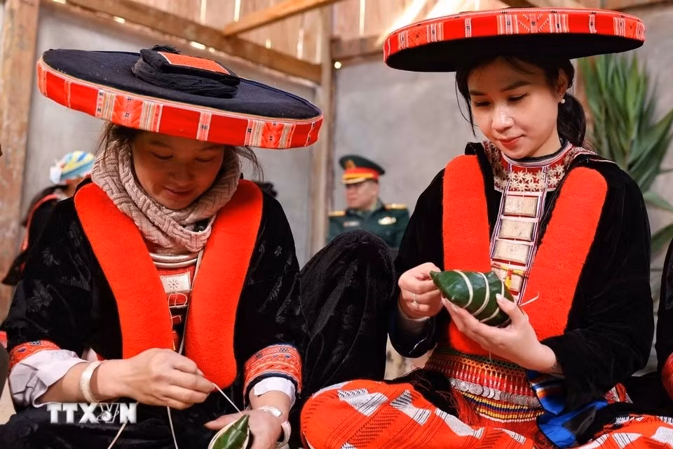 Une touriste hanoïenne (droite), vêtue d'un magnifique costume traditionnel Dao Rouge du district de Nguyen Binh, s'initie avec passion à l'art ancestral de l'emballage des banh chung gù. Contrairement au banh chung carré, le banh chung gù a une forme plus arrondie, légèrement bombée au centre, d'où son nom "gù" qui signifie "bossu" en vietnamien. (Photo : Thanh Tung/VNA)