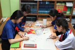Des élèves de l'école bilingue lao-vietnamienne Nguyen Du dessinent un tableau sur l'Oncle Hô. Photo : VNA