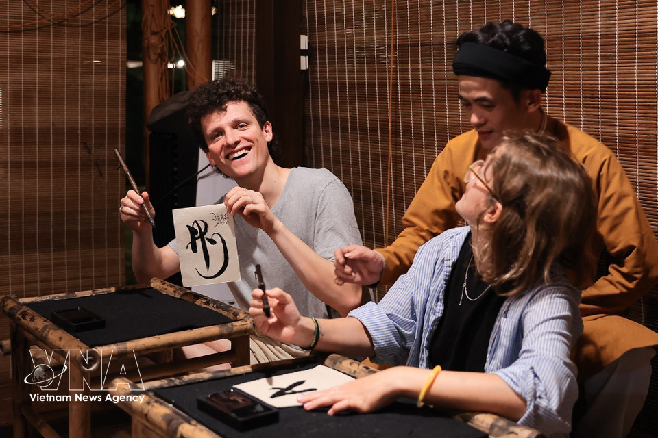 Des touristes étrangers s'initient à la calligraphie lors de leur visite nocturne du Temple de la Littérature. Photo: VNA