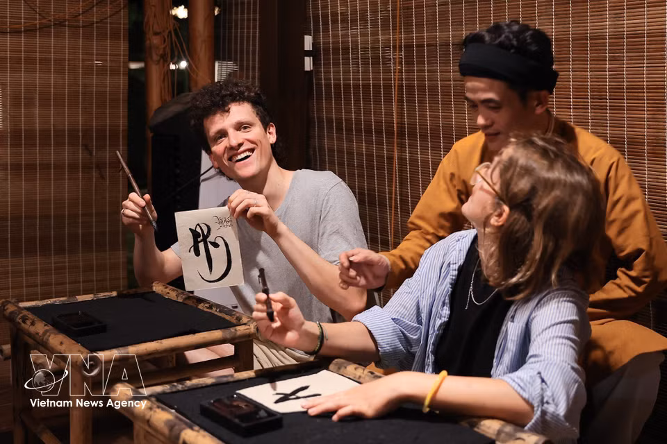 Des touristes étrangers s'initient à la calligraphie lors de leur visite nocturne du Temple de la Littérature. Photo: VNA