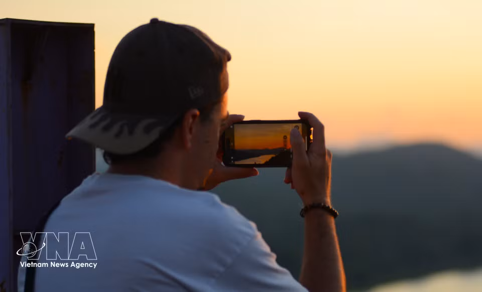 Un touriste étranger immortalise les paysages environnant la colline de Vong Canh à l’heure du coucher du soleil. Photo: VNA
