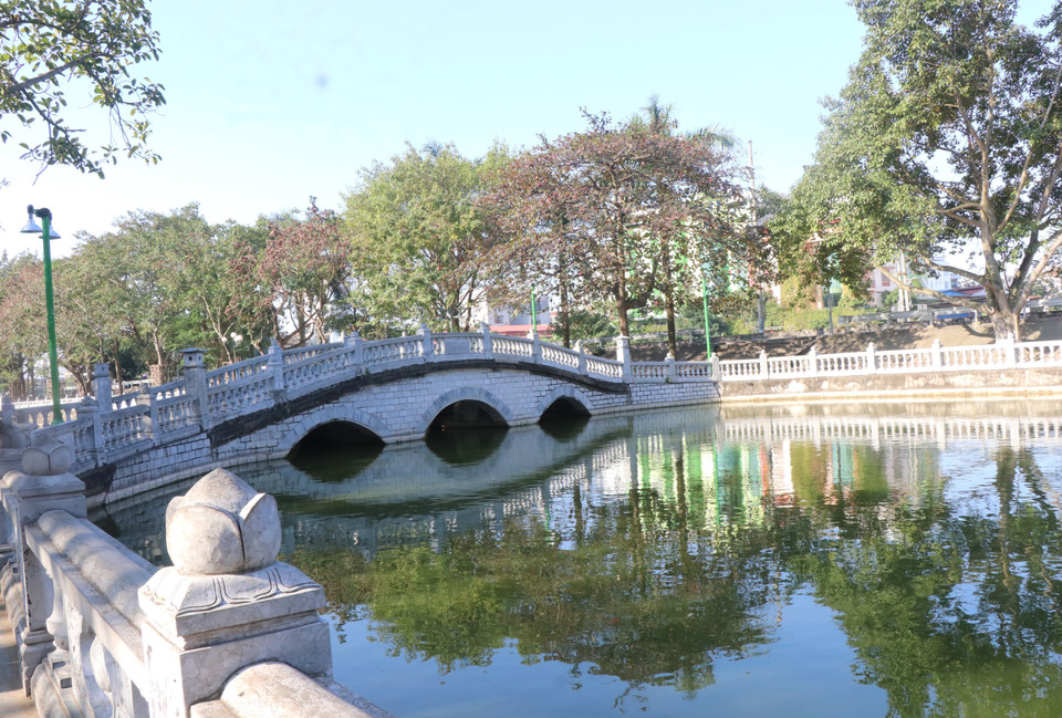 Devant la maison communale s'étend un grand étang bordé de pierres, agrémenté de deux élégants ponts en pierre bleue aux arches harmonieuses, créant un paysage serein et aéré. Photo: VNA