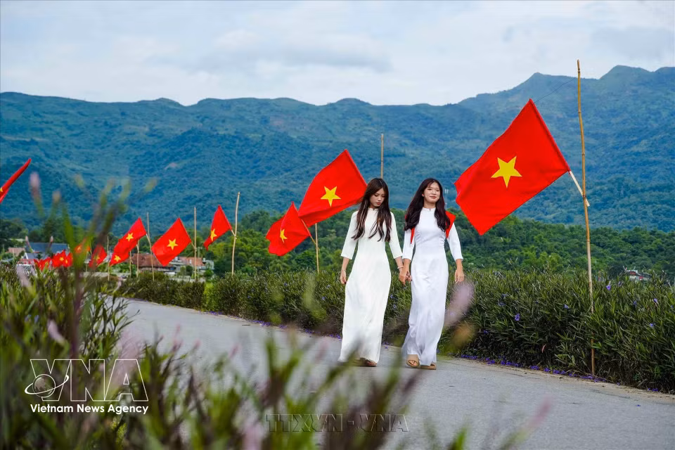 Deux étudiantes vêtues de l’ao dài (tunique traditionnelle) marchent au milieu d’une profusion de drapeaux nationaux dans la plaine de Muong Thanh.