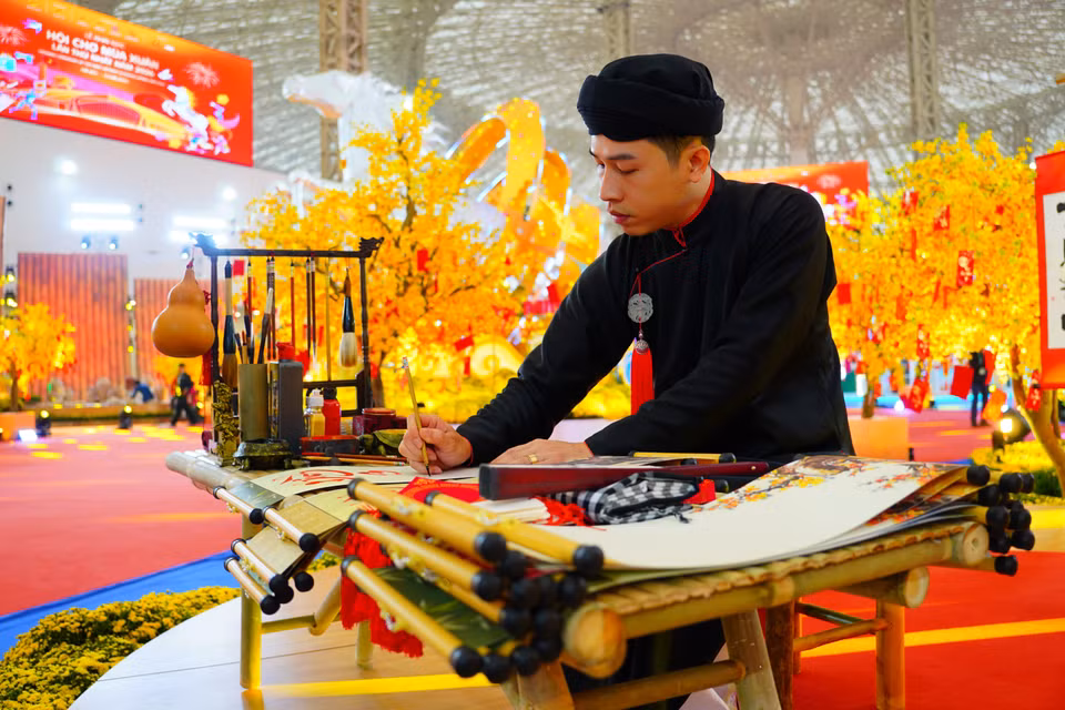 Un maître calligraphe, vêtu du costume traditionnel, s'exerce à son art devant les visiteurs. Photo : VNA
