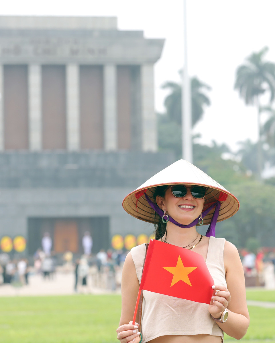 Une touriste étrangère pose pour une photo souvenir avec le drapeau national vietnamien. Photo : VNA