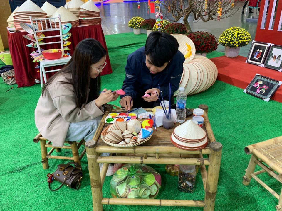 Des visiteurs décorent des chapeaux coniques à la foire. Photo : VNA