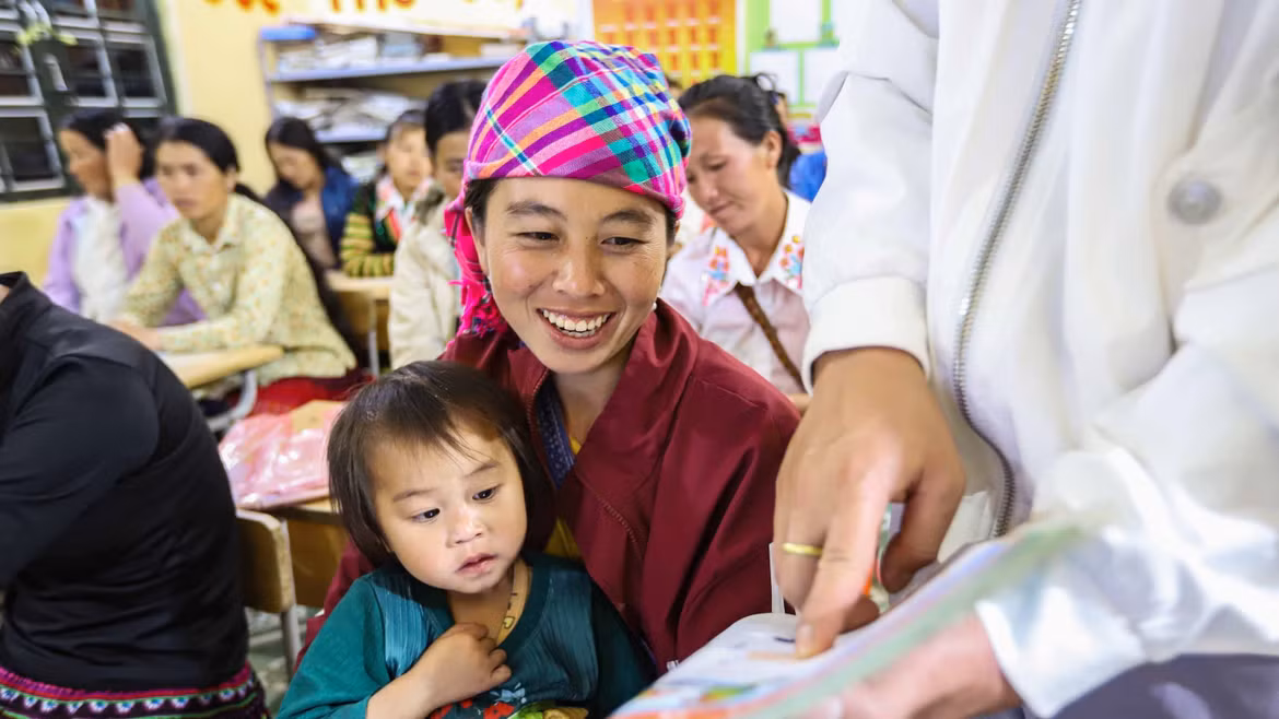 Hang Thi Cha, accompagnée de sa fille, s’exerce à la lecture avec son enseignant à l’aide d’un manuel de vietnamien de première année. Photo : VNA