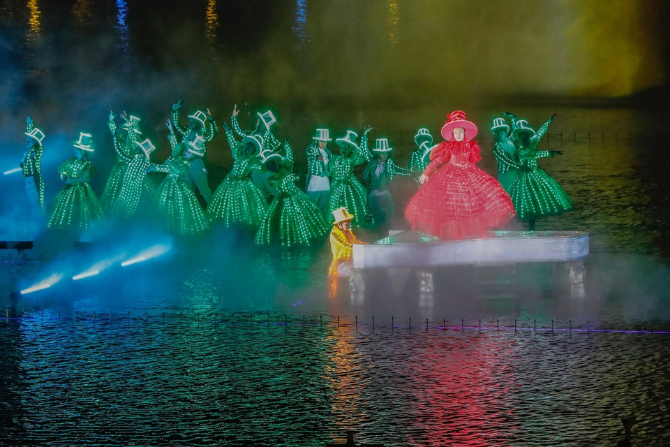 Des artistes masqués, vêtus de costumes sophistiqués équipés de lumières LED, se produisent sur une scène flottante au milieu de l'eau, créant une atmosphère de carnaval à Venise. 
