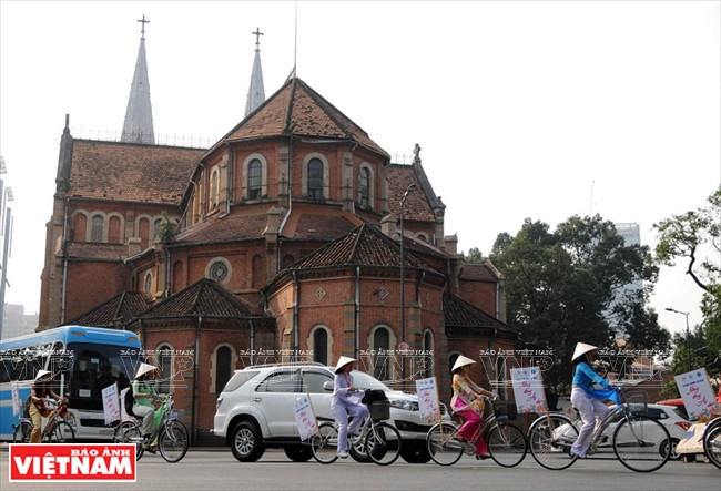 Les filles portant l’Ao dài participent à un défilé à vélo en passant par la Cathédrale Notre Dame de HCM-Ville.