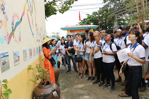 Les jeunes membres du Forum des Voix du futur s’informent sur les dessins muraux dans le village Bich Hoa.