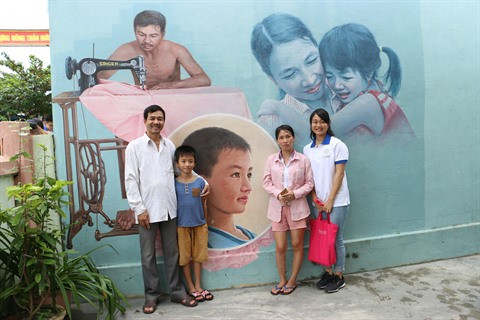 Une jeune déléguée prend une photo souvenir avec une famille du village devant le mur dessiné de sa maison.