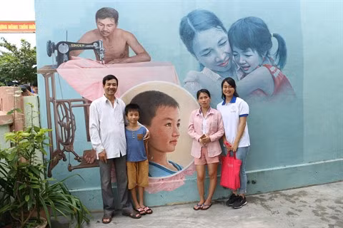 Une jeune déléguée prend une photo souvenir avec une famille du village devant le mur dessiné de sa maison.