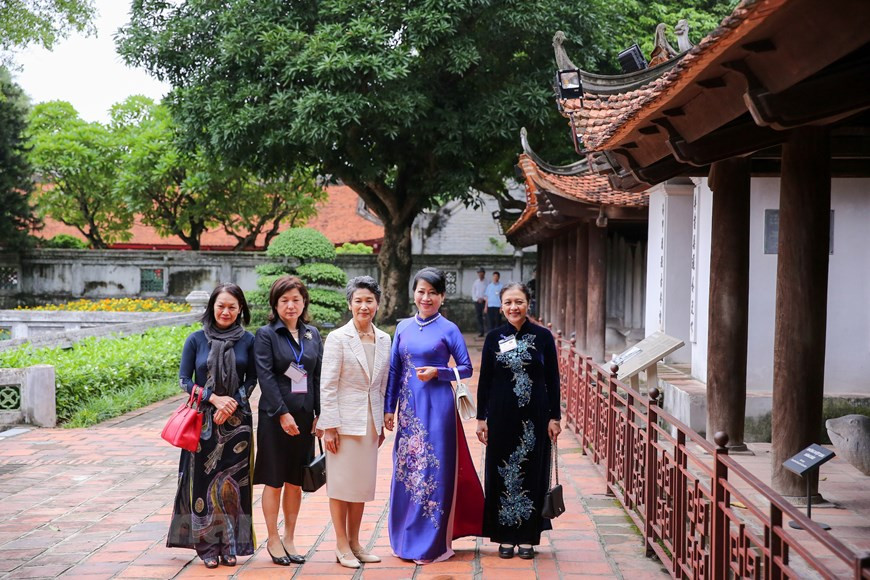 Les deux femmes et des délégués sont guidés pour visiter les sites dans le temple. À l'époque de la dynastie Trân (1225 à 1400), le temple a été remanié à maintes reprises avec une succession de démolitions et de reconstructions. Il est inscrit aux Monuments historiques en 1906. Il a été entièrement restauré en 1920 et en 1947 grâce aux travaux de l'École française d'Extrême-Orient. Mais ensuite, endommagé par la guerre d'Indochine, il a de nouveau été restauré en 1956. La dernière campagne de restauration remonte à l'an 2000. C'est aujourd'hui l'un des points d'attraction culturelle et touristique majeurs de la capitale vietnamienne. 