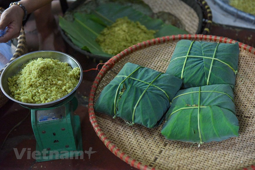  À Hanoï, le côm est vendu un peu partout : dans les rues, les marchés... Les graines de riz vertes décortiquées et pilées sont placées dans un panier en bambou tressé sur lequel sont préalablement disposées de larges feuilles de lotus fraîches. En fonction de la commande du client, la vendeuse enveloppe une quantité - souvent de 100 grammes, 200 grammes... et jusqu’à un kilo - au milieu d’une feuille de lotus fraîche sous la forme d’un paquet carré ficelé à l’aide de brins de paille de riz. Le prix du côm vendu au village de Me Tri varie entre 170.000 et 200.000 dongs le kilogramme. Photo: VietnamPlus