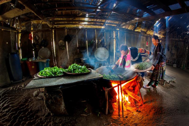 Vang A Khua et sa femme mettent les bourgeons de thé dans une casserole et les font griller sur un poêle à bois.