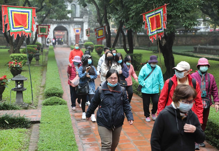 En se rendant au Temple de la Littérature, des touristes portent des masques de protection pour la prévention et la lutte contre l'épidémie du coronavirus. Photo: VietnamPlus
