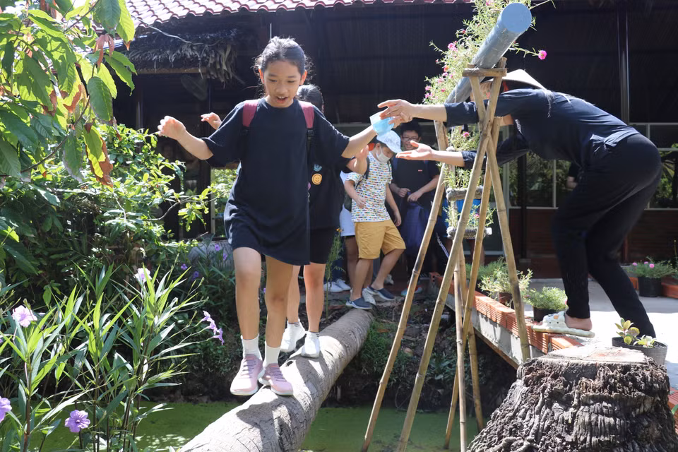 Les jeunes touristes profitent de l'expérience de marcher sur un pont de cocotiers dans le jardin de cacaoyers de la Sarl de cacao Xuan Ron Cho Gao. Photo:VNA