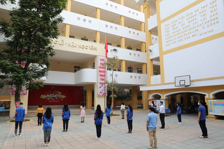 Au lycée Tran Nhan Tong, des enseignants et élèves participent à une cérémonie de salut au drapeau national tout en appliquant la distanciation sociale. Photo: VNA