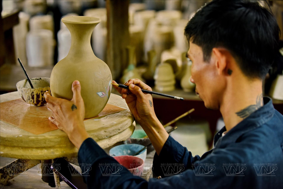Un artisan décore un vase en céramique avec des motifs.