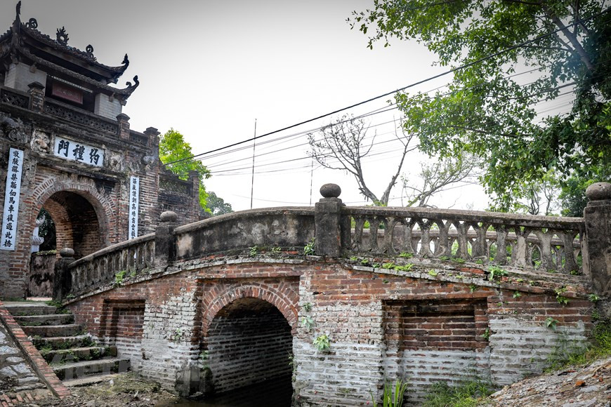 C’est par un pont arqué de deux mètres de large et de dix mètres de long que l’on entre dans le village. Précédemment, le fossé situé en dessous du pont est une tranchée profonde entourant tout le village, où étaient plantés des arbres de bambous. Cette tranchée fait ainsi office de mur de protection conte les voleurs. Mais ce qui distingue particulièrement ce village des autres est son portique d'entrée. Il délimite véritablement l’espace à l’intérieur duquel se tisse la trame d’une vie communautaire régie par toute une série de règles, aussi tacites qu’immuables. Le portique d'entrée du village était aussi un lieu de garde afin de décourager de toute intrusion. Photo: Vietnamplus