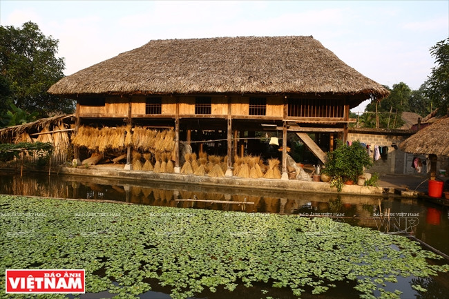 Une maison typique en bois des Tày dans le hameau de Tha avec le toit en feuilles de palmier et les étangs piscicoles.